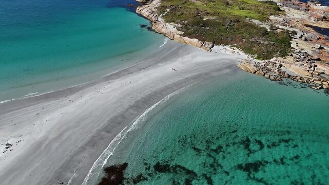 People arriving famous Diamond Island in Tasmania after walk over sandy path between clear ocean water. TIlt up wide shot scene in summer.