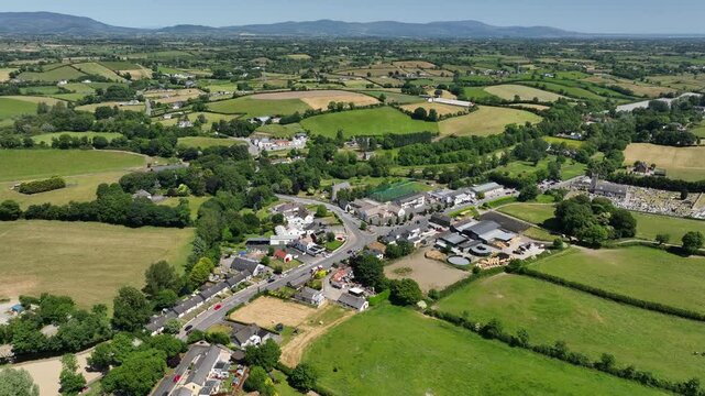 Inniskeen Village, County Monaghan, Ireland, June 2023. Drone orbits clockwise above intersection connecting the village center amidst rolling green fields.