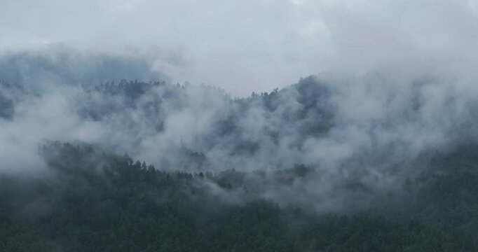 Drone shot of misty clouds flowing freely over the hills of Nepal in the evening after the monsoon rain season. The scene features a cold, lonely atmosphere with a filmy, serene scenario.