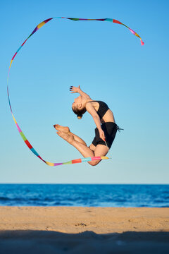 Young woman performing rhythmic gymnastics with ribbon on a beach