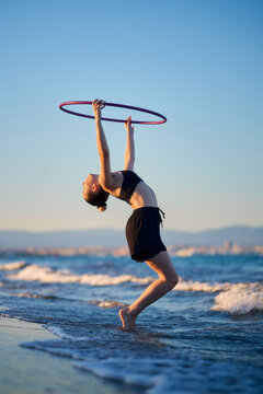 Woman hula hooping near the shore during sunset at the beach
