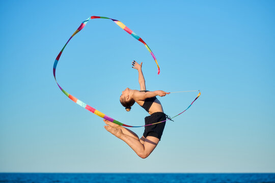 Young woman performing rhythmic gymnastics with ribbon on a beach