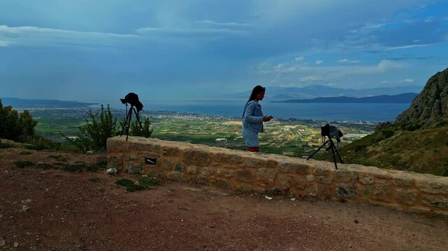 Aerial shot revealing beautiful landscape of Corinth city from Acrocorinth Castle at Greece. Female tourist with cameras at foreground.