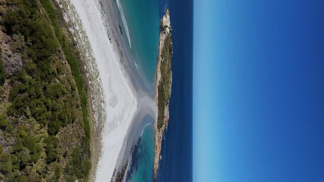 Vertical drone backwards shot of Diamond Island with sandy beach on coastline of Tasmania in summer. Blue sky with vibrant colors of sea.