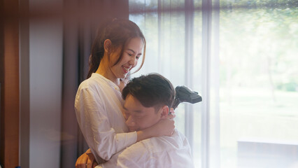 Young adult couple two asia people relax joy smile blow hair dryer spend good time at cozy home...