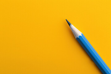 Sharpened blue pencil on a solid yellow background, showcasing strong color contrast in a bold and minimalist design.