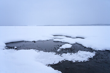 Obraz premium Snow-covered landscape with open water patches in a frozen lake