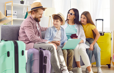 Happy family of four with kids buying tickets and booking hotel online using laptop sitting on sofa in living room at home with packed suitcases planning summer vacation. Holiday trip concept.