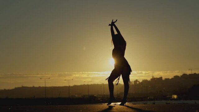 Woman is dancing salsa alone on a rooftop at sunset