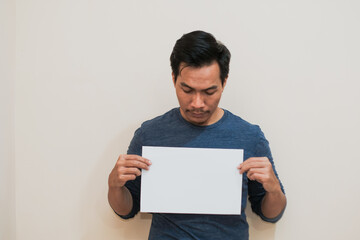 Serious Portrait of Southeast a Asian man activist holds piece of blank sheet of paper sign in his hands standing on cream background.