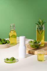 Mockup scene for cosmetic product of olive extract with white bottle without label decorated on white background with many flasks of olives. Advertising photo, minimal concept.