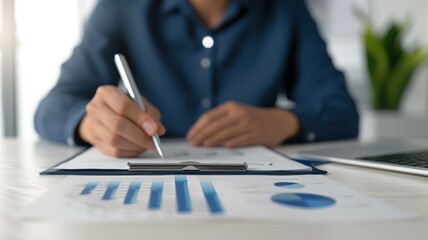 Fototapeta premium A professional analyzing data, writing notes on a report with graphs and charts on a desk alongside a laptop.