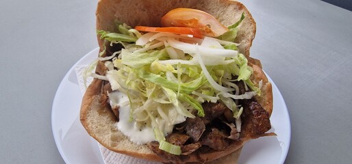 Doner kebab pocket on a plate with lettuce, tomatoes and sauce