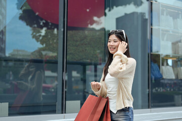 Cheerful asian woman carrying shopping bags walking in the city street