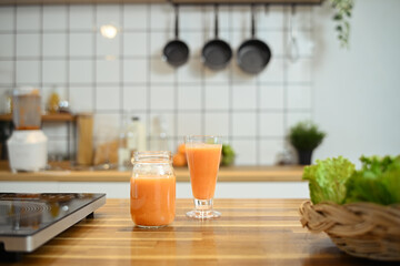 Two refreshing glass of orange juice sitting on a wooden table in a kitchen