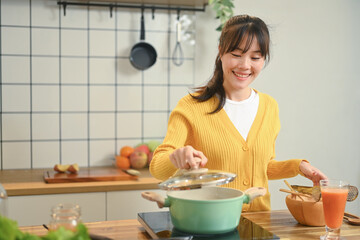 Pretty young woman in a light yellow cardigan is enjoying cooking in the kitchen at home