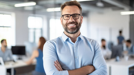 Fototapeta premium A handsome man in his thirties, wearing glasses and a blue shirt is standing with his hands crossed smiling at the camera.