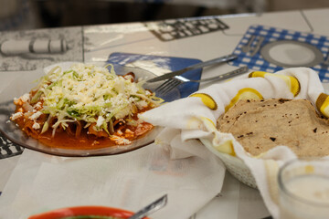 Plate of authentic Mexican enchiladas topped with cheese and lettuce, served alongside a basket of fresh homemade tortillas, traditional recipe from a Mexican restaurant in a cultural market