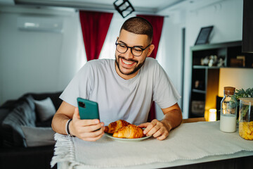 Young caucasian man eating croissant for breakfast