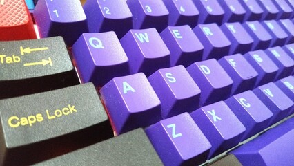 A detailed close-up of a vibrant purple mechanical keyboard featuring black "Caps Lock" and "Tab" keys with yellow labels. The image highlights the tactile texture of the keys, perfect for tech or gad © artofangga