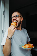 Young caucasian man eating croissant for breakfast