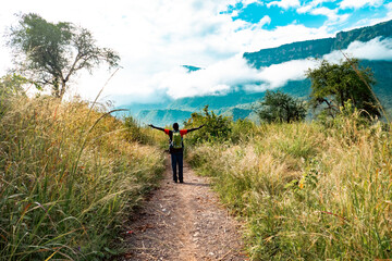 Rear view of a hiker on a dirt road amidst savannah grassland against the background of Mount Napak in Karamoja, Uganda
