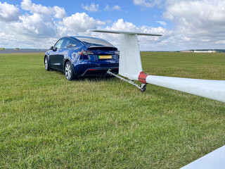 Blue EV electric car with tow bar towing a glider on an airfield blue sky and white cumulus clouds