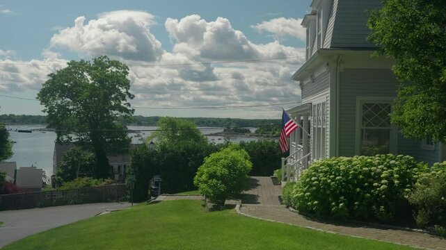 Hingham, MA, USA. June 16, 2024. New England style wooden house on a hill with US flag and view of bay. 