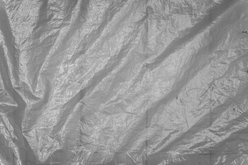 A close-up of a wrinkled plastic and foil texture, featuring crumpled patterns and a mix of silver and black hues. The grunge element adds an abstract, reflective quality to the material.