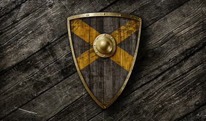 Medieval triangular wooden shield with golden hand forged brim and yellow and black pattern design on ancient diagonal wooden background