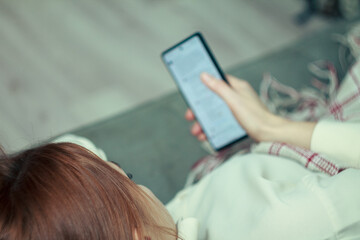 Fototapeta premium The girl is procrastinating: lying with a phone in her hands, a lazy expression on her face, a concentrated look