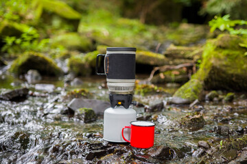 Coffee pot and metal cup on a large stone against the background of a mountain river. Coffee pot on...