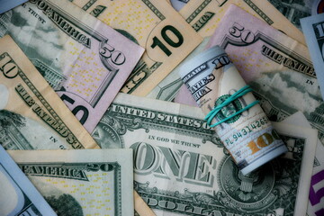 Hundred dollar bills roll lies on big amount of US dollars in different nominations under natural light