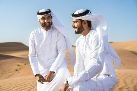 Two middle-eastern emirati men wearing arab kandura bonding in the desert