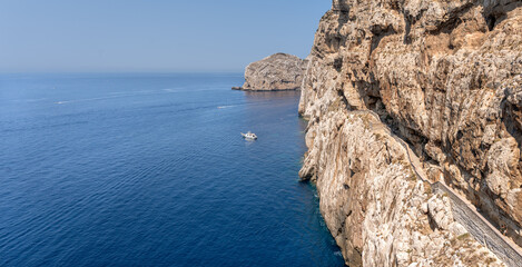 Spectacular seascape of the great cliff with access to the Neptune's Grotto (Grotta di Nettuno) dug in the middle of the cliff in Sardinia, overlooking the deep blue of the Mediterranean Sea