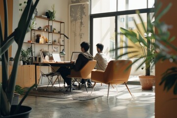 Naklejka premium Two individuals working on computers in a stylish and airy home office, surrounded by plants and sunlight streaming through the large windows.