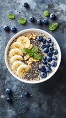 Smoothie bowl with banana, blueberries, chia seeds and oat flakes decorated with mint leaves on blue background. Healthy breakfast