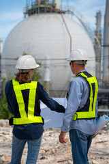 Team Petroleum chemical engineer discussion about blueprint drawings inside Oil Refinery Gas Chemical site. Senior Engineer wearing safety jacket and PPE working about Petro Chemical plant