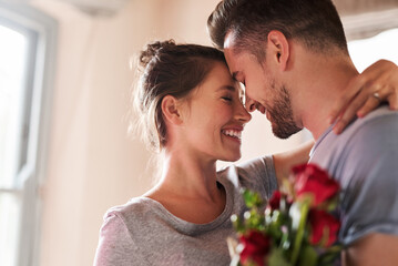 Flowers, happy couple and hug in home for love, connection and bonding together with present. Affection, man and woman with red roses for relationship, commitment or anniversary celebration in house