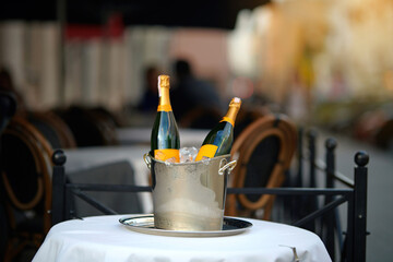 Chilled champagne bottles in an ice bucket on a table at an outdoor restaurant terrace. Champagne on ice, bottles chilling in bucket on the outdoor terrace of fine dining restaurant