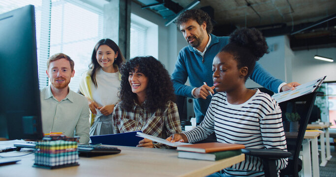 Multi-ethnic group of people gathering in front on large monitor. People working together in big office room. Cooperating. Discussing possible ways of improvement for firm. Business meeting.