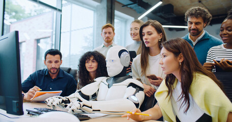 Multi-ethnic group of smart engineers looking at their robot entering text. Checking if program or...