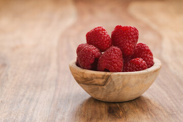 fresh raspberries in wood bowl on table with copy space