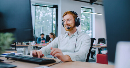 Camera focus on handsome Caucasian male sitting at desk. Putting on wired headphones with microphone. Beginning conversation with client or company. Technical support department. Smiling with joy.