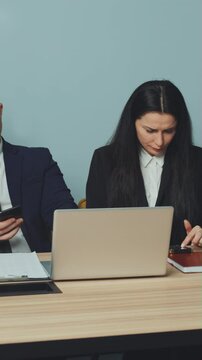 Vertical Screen: business professionals seated at table during break, each engrossed in their smartphones. Prevalence of mobile addiction and distraction in corporate setting. Concept of work break