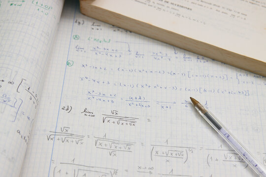 Close-up of advanced math homework next to a student's pen and book