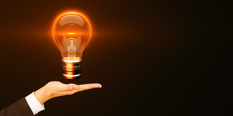 Hand presenting glowing lightbulb on dark background, symbolizing creativity and innovative ideas.