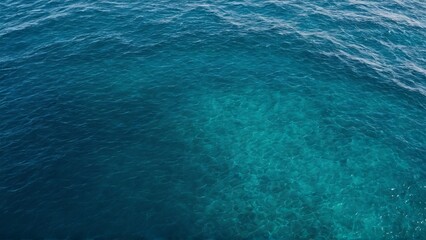 Obraz premium Aerial view of a clear turquoise ocean with gentle waves. The sunlight creates a beautiful pattern on the surface, showcasing the vibrant shades of blue and green in the water