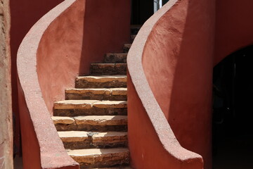 Vue d'un détail de l'escalier de couleur orangée de la maison des esclaves de l'île de Gorée au Sénégal. Rampe de forme incurvée. Architecture coloniale. Bâtiment rénové et coloré. Avril 2024.