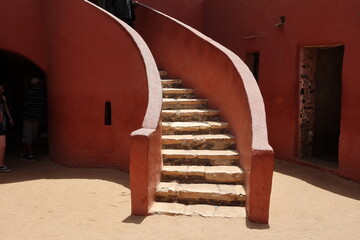 Vue d'un détail de l'escalier de couleur orangée de la maison des esclaves de l'île de Gorée au Sénégal. Rampe de forme incurvée. Architecture coloniale. Bâtiment rénové et coloré. Avril 2024.